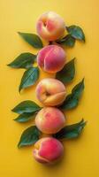 Vibrant peaches arranged with green leaves on a bright yellow background in a modern aesthetic display photo