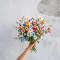 Hand holding a vibrant bouquet of wildflowers against a light background in daylight photo