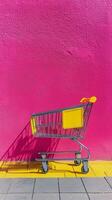Shopping cart in front of vibrant pink wall on sunny day at urban location photo