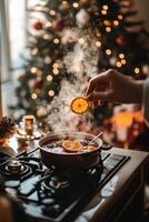 Festive holiday beverage preparation with spices and citrus near a decorated Christmas tree photo