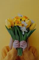 Bright and cheerful woman holding a bouquet of yellow daffodils against a soft yellow background photo