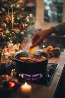 Festive holiday beverage preparation with spices and citrus near a decorated Christmas tree photo