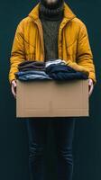 Person holding a box of clothes for donation in a forested area during an overcast day photo