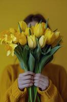 Bright and cheerful woman holding a bouquet of yellow daffodils against a soft yellow background photo