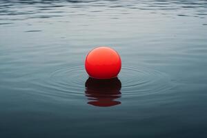Red buoy floating on calm water with ripples radiating outward in early morning light photo