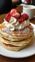 Stack of fluffy pancakes topped with whipped cream and fresh strawberries in a cozy cafe photo