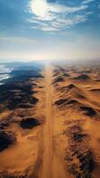 Expansive desert landscape featuring winding road surrounded by sand dunes and distant mountain range photo