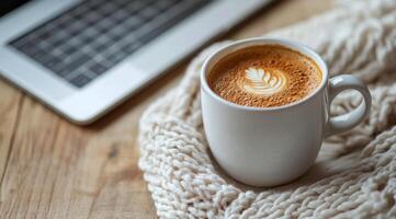 Warm coffee cup with latte art on a cozy knitted blanket beside a laptop photo