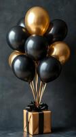 Celebration decoration featuring black and gold balloons with a gift box on a gray background photo