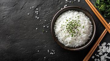 Delicious white rice served in a bowl with chopsticks and fresh herbs on a dark background photo
