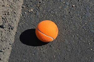 Bright orange tennis ball resting on a textured dark surface in a dramatic setting photo