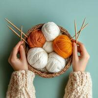 Hands holding a basket of yarn in various colors with knitting needles on a teal background photo
