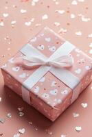 Gift box adorned with hearts surrounded by sparkly confetti on a soft pink background photo