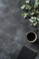 Cozy workspace setup with coffee cup, notebook, and greenery on black background photo