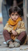 Young boy sitting cross-legged on the street wearing a warm scarf and sweater in a busy urban area photo