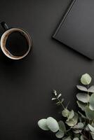 Cozy workspace setup with coffee cup, notebook, and greenery on black background photo