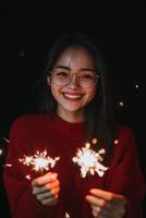 Celebratory young woman holding sparklers in cozy red sweater against dark background photo