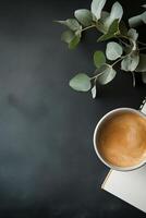 Cozy workspace setup with coffee cup, notebook, and greenery on black background photo