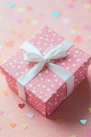 Gift box adorned with hearts surrounded by sparkly confetti on a soft pink background photo