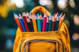 Colorful pencils in a yellow backpack against a blurred outdoor background during daytime photo