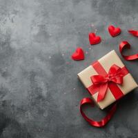 Gift wrapped in beige paper with red ribbon and hearts on dark textured background photo