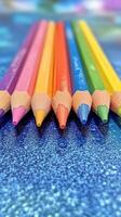 Colorful pencils arranged in a vibrant pattern on a glittery blue surface photo
