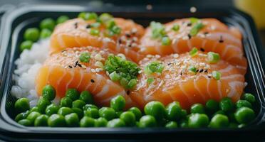Fresh salmon sashimi served over rice with green peas in a black container photo
