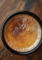 Rich brown beverage in a dark ceramic cup placed on a textured wooden surface photo