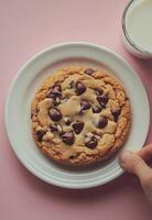 Delicious chocolate chip cookie on a white plate held above a glass of milk photo