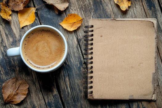 Warm coffee and notebook resting on wooden table with autumn leaves scattered around photo