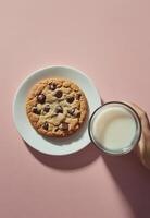 Delicious chocolate chip cookie on a white plate held above a glass of milk photo