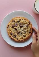 Delicious chocolate chip cookie on a white plate held above a glass of milk photo