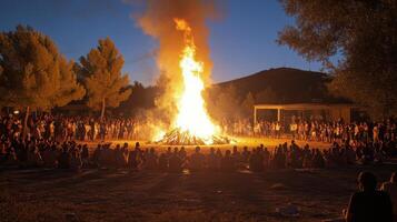 Crowd gathered around a large bonfire during an evening celebration in a natural setting photo