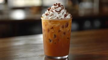 Iced coffee topped with whipped cream and chocolate, surrounded by snacks on a wooden table photo