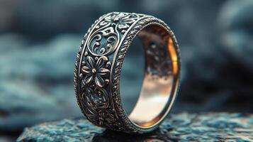 Intricate silver ring with floral motifs displayed on a textured stone surface photo