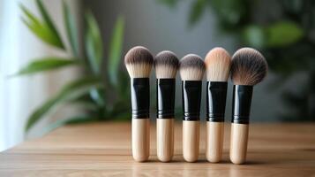 Variety of makeup brushes arranged neatly on a wooden surface near green plants photo