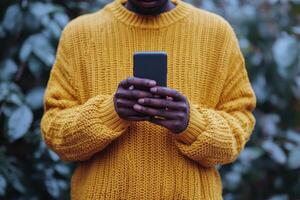 Stylish man in a yellow sweater uses smartphone in a lush outdoor setting during daytime photo