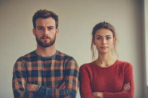 Young couple poses together in a neutral space with crossed arms and serious expressions photo