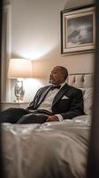 Confident man in a suit sitting on a bed in a dimly lit hotel room during evening hours photo