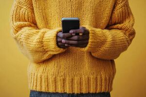 Stylish man in a yellow sweater uses smartphone in a lush outdoor setting during daytime photo
