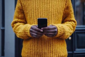 Stylish man in a yellow sweater uses smartphone in a lush outdoor setting during daytime photo