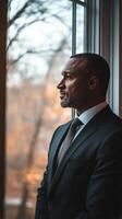 Business professional in suit gazing thoughtfully out of window during golden hour photo