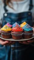 Colorful cupcakes with bright frosting displayed on a plate by a person in casual attire photo