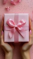 Gift wrapping with pink bow held in hands against a dark textured background during a festive celebration photo