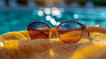 Sunglasses resting on a towel beside a sparkling pool under a bright sunlit sky photo