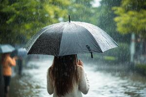 Woman enjoying autumn rain under a black umbrella in a park with vibrant yellow leaves photo