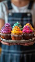 Colorful cupcakes with bright frosting displayed on a plate by a person in casual attire photo