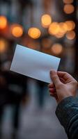 Hand holding a blank card in a bustling street adorned with soft, glowing lights photo
