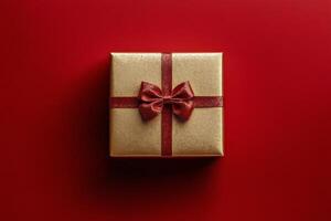 Shimmering gold gift box with red ribbon on vibrant red background ready for a special occasion photo
