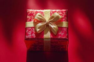 Shimmering gold gift box with red ribbon on vibrant red background ready for a special occasion photo